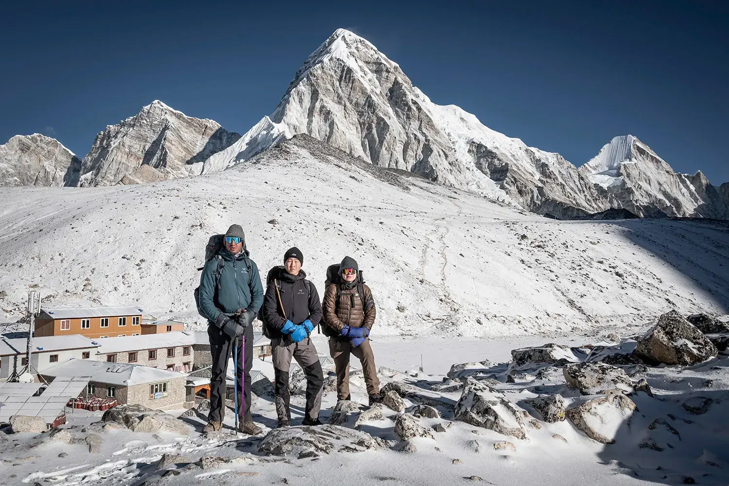 Three trekkers standing near Gorakshep with snow-covered Mount Pumori in the Everest region of Nepal.