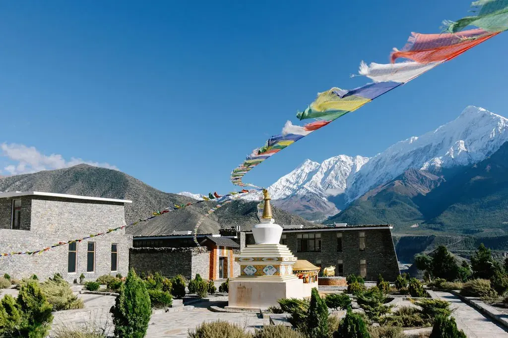 Buddhist stupas and colorful prayer flags with snow-capped Himalayan mountains viewed from Shinta Mani Mustang in Upper Mustang, Nepal.